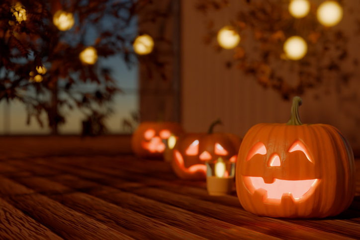 Glowing Halloween jackolanterns lined up on a wooden floor with warm festive lights behind them. 3d rendering